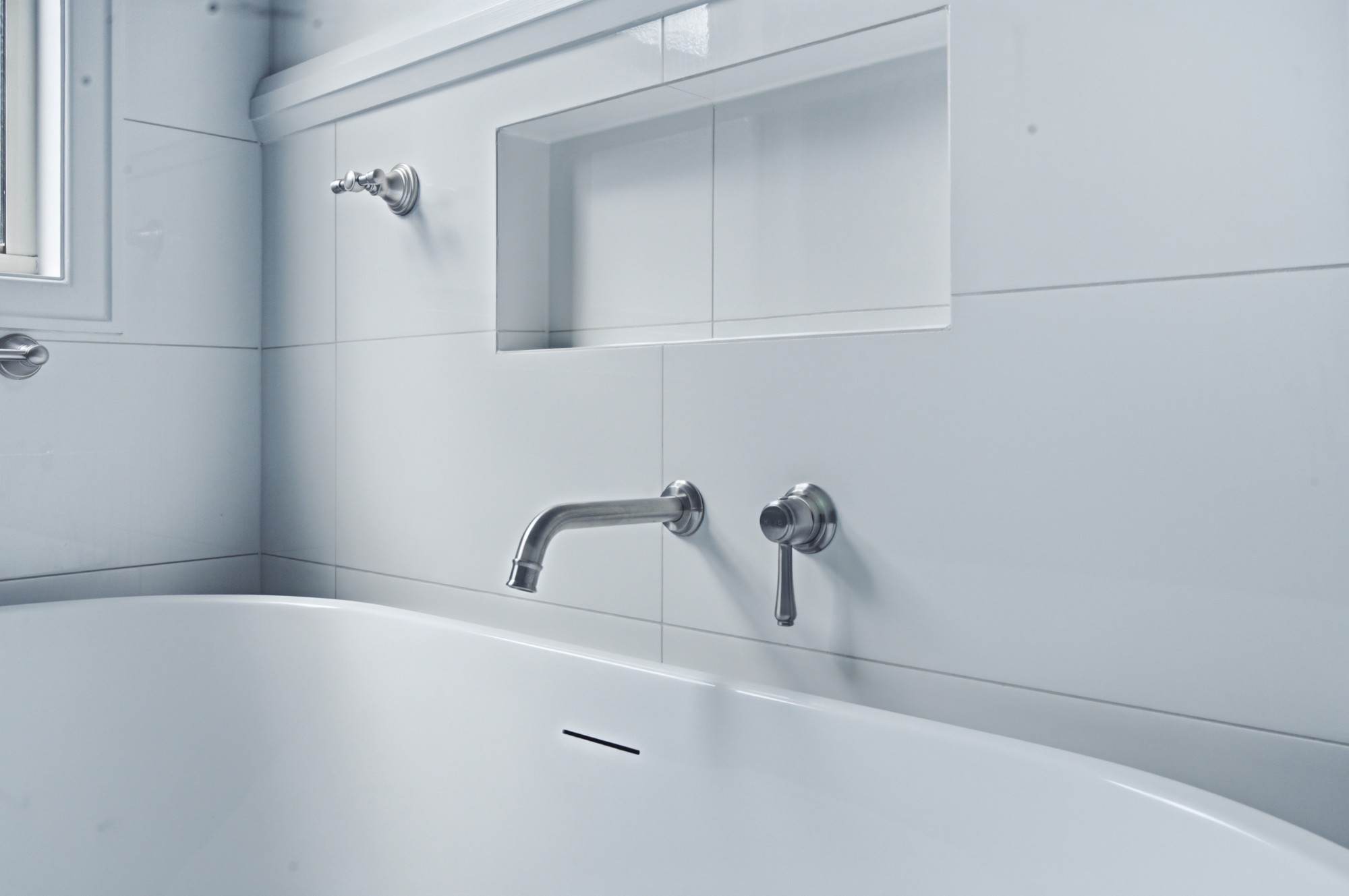 Close detail of wall-mounted bath spout and mixer against white tiles