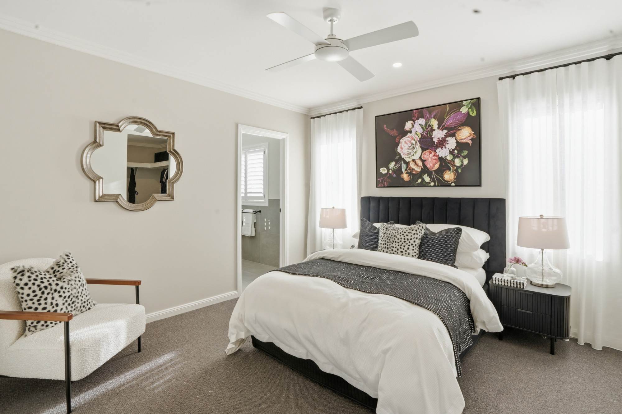 Master bedroom with velvet headboard, floral artwork and ensuite beyond