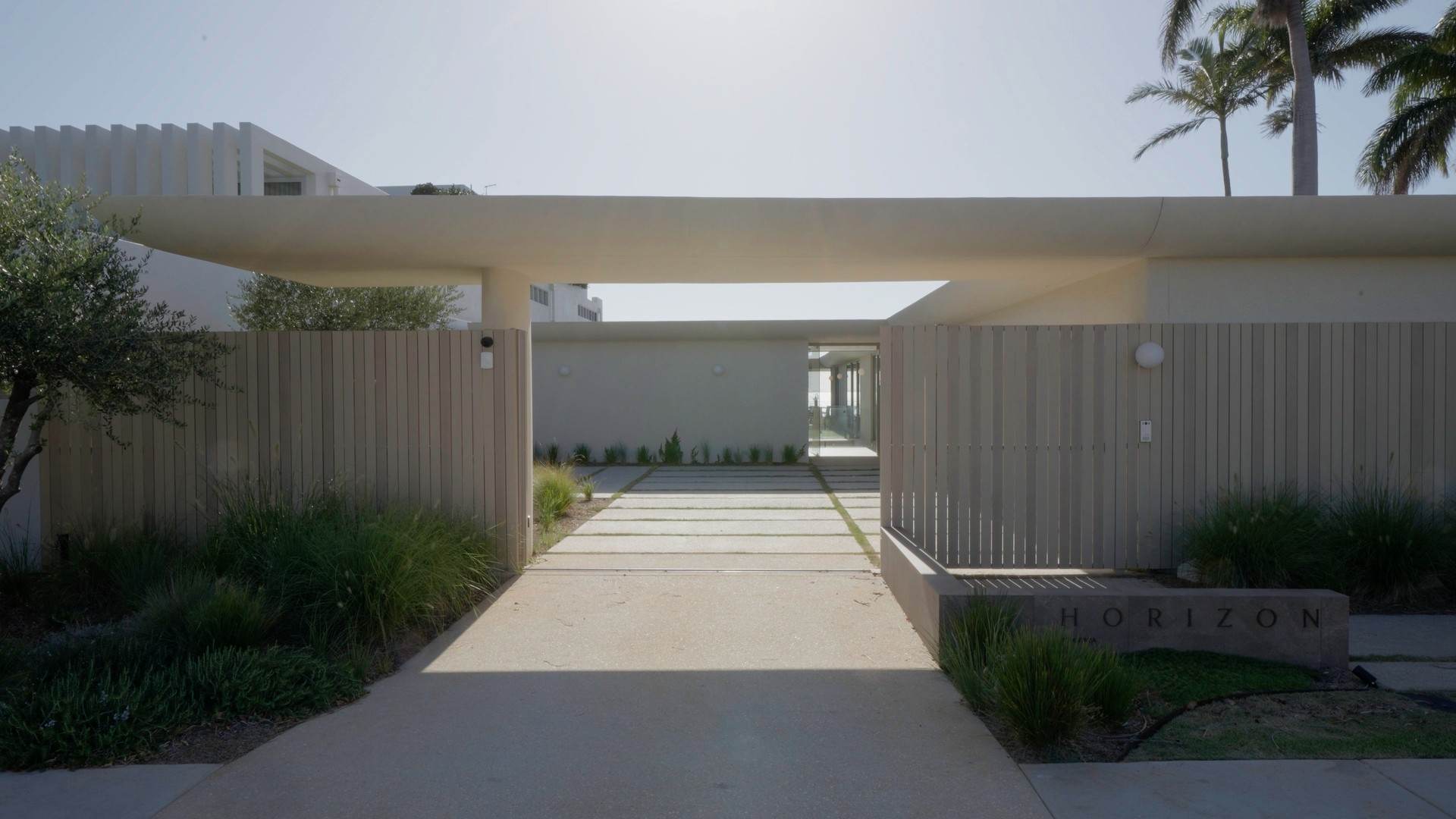 Street entry with slatted timber gates under a sweeping concrete canopy and HORIZON signage
