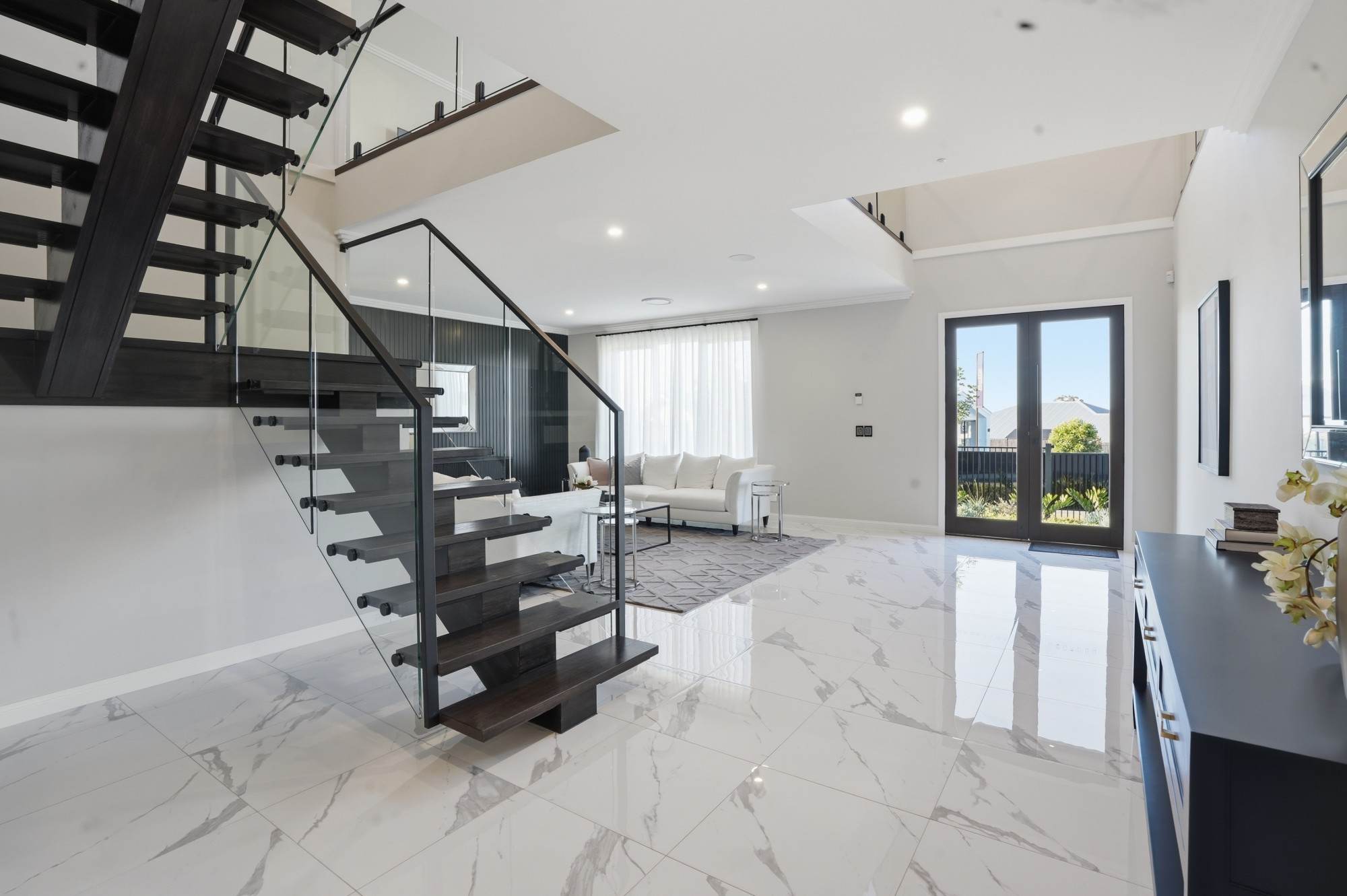 Display home entry with floating timber staircase, glass balustrade and marble-look tiles