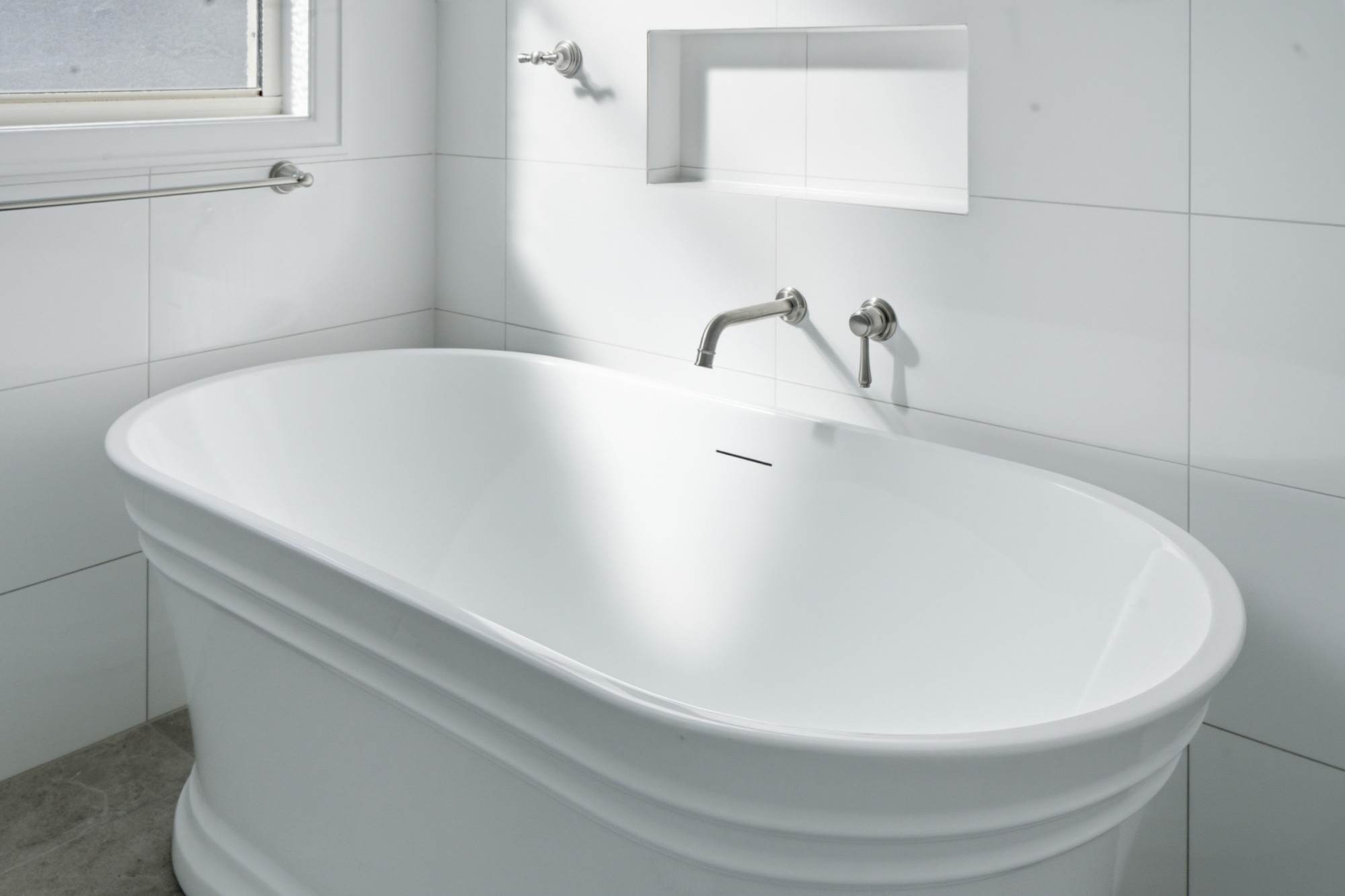 Freestanding bath with wall-mounted brushed nickel spout and tiled niche