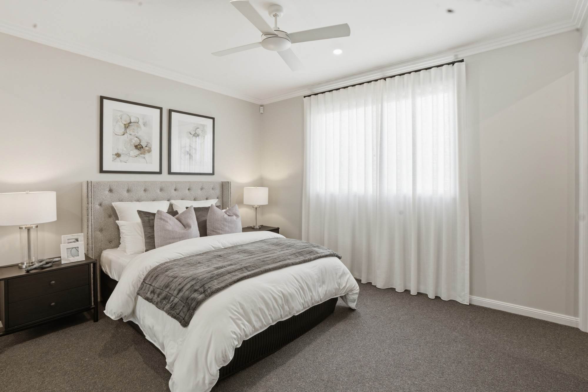 Guest bedroom with tufted headboard, framed prints and full-height sheer curtains