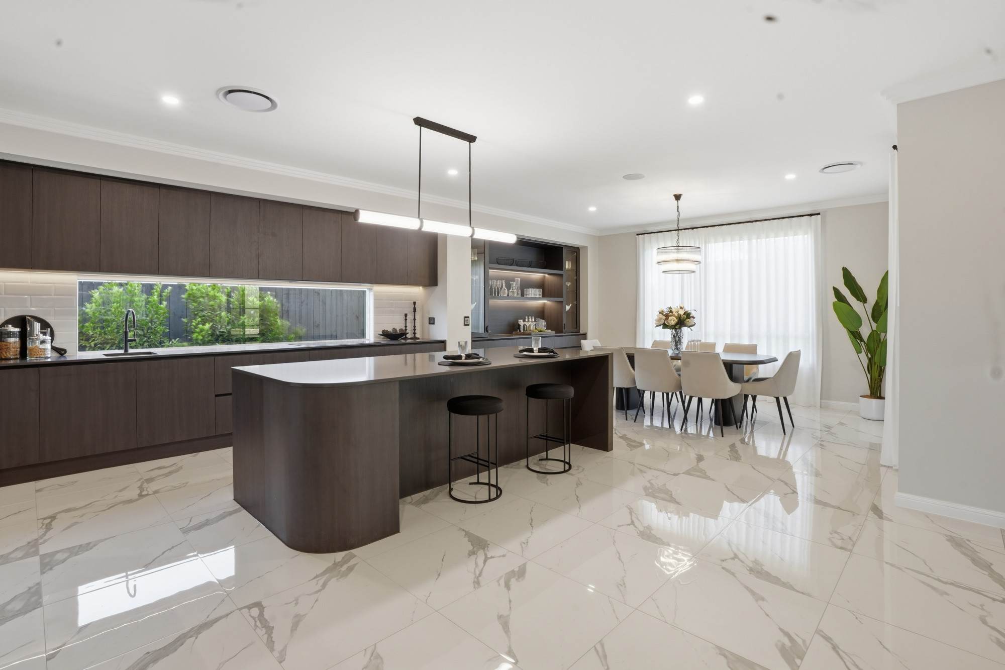 Kitchen with window splashback, curved island and dining beyond