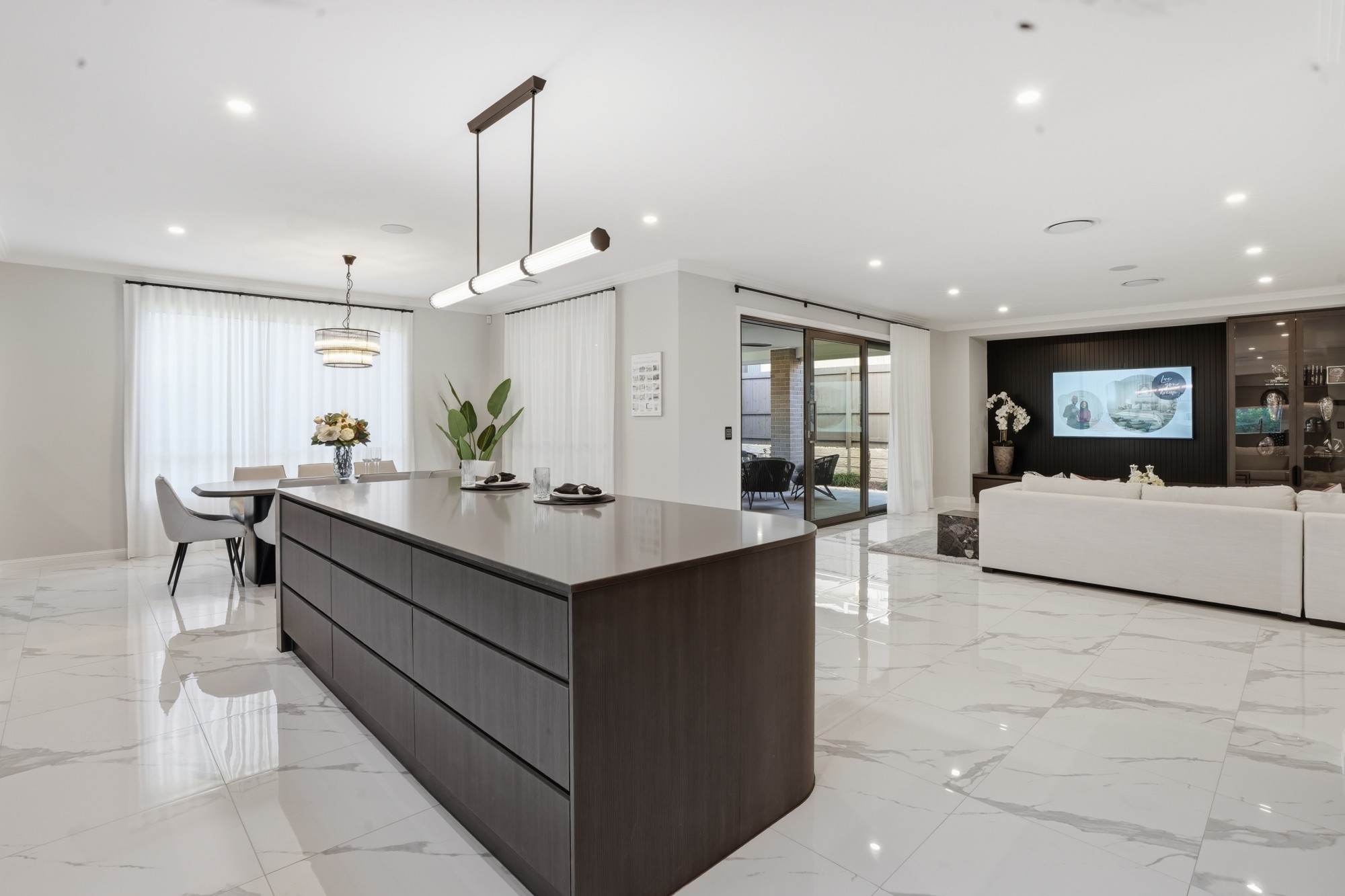 Display home kitchen with curved timber island, linear pendant and marble-look floor tiles