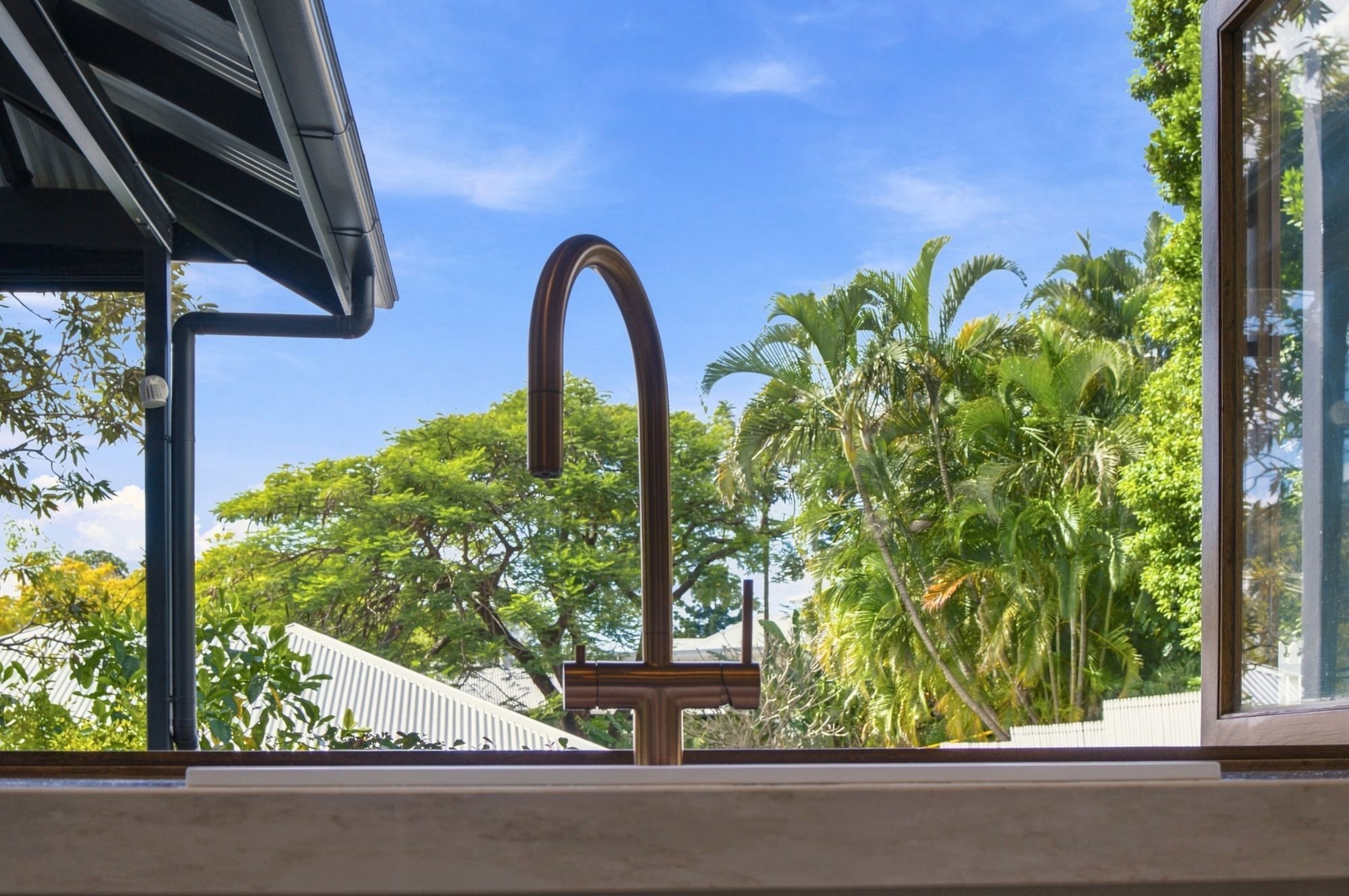 Kitchen tap framed by an open window and a lush green garden