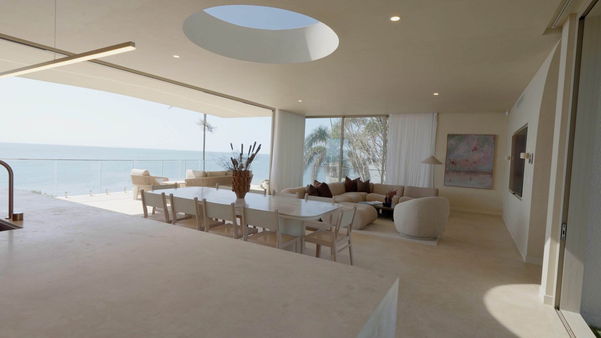 Open-plan living and dining under a circular skylight, opening to a glass balcony over the bay