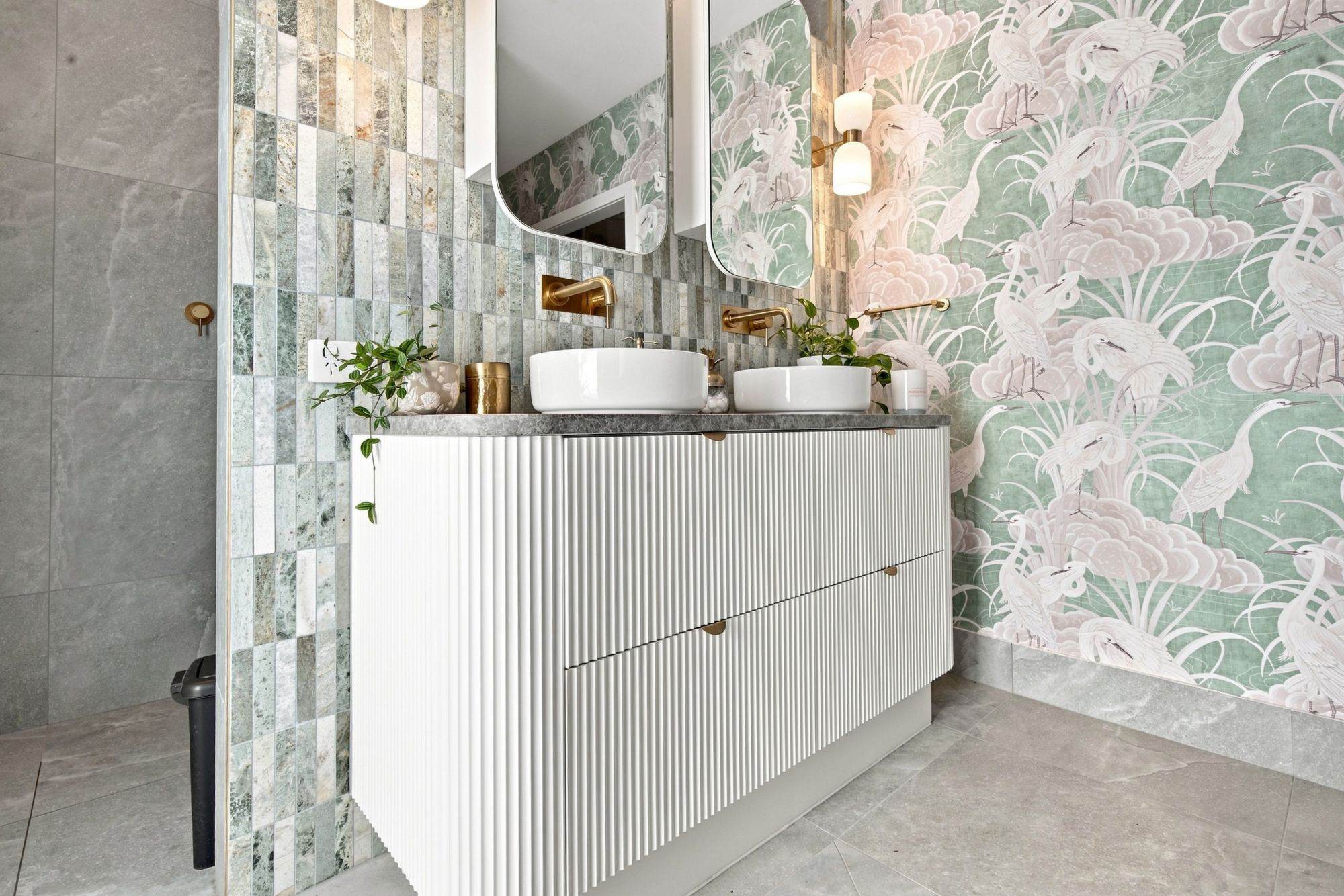 Fluted white vanity beside heron-print wallpaper and stone mosaic tiles